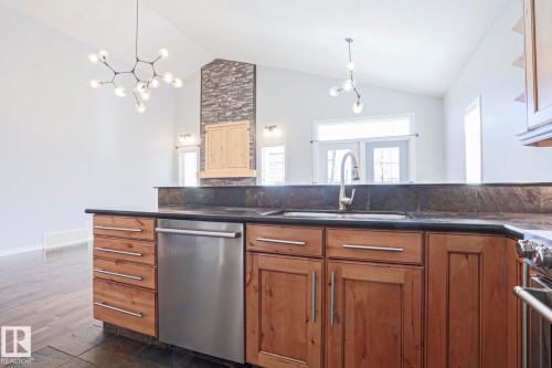 The kitchen features wooden cabinetry with a stainless steel dishwasher, a sink with a gooseneck faucet, and dark countertops - 205 79 Street Sw, Edmonton, AB - Indoor Photo Showing Kitchen