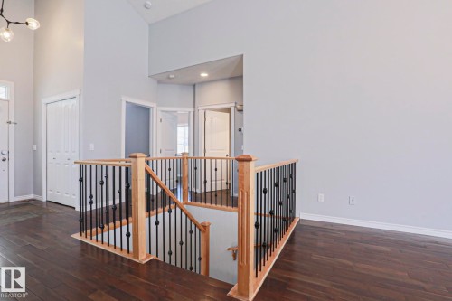 This property features hardwood floors, a staircase with light wood banisters and dark metal spindles, and white walls - 205 79 Street Sw, Edmonton, AB - Indoor Photo Showing Other Room