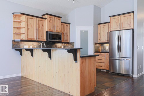 Kitchen featuring wood cabinetry, a stainless steel refrigerator, and a built-in microwave - 205 79 Street Sw, Edmonton, AB - Indoor Photo Showing Kitchen