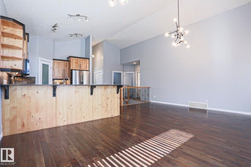 This open-concept area features dark hardwood flooring, a vaulted ceiling, and a modern light fixture - 205 79 Street Sw, Edmonton, AB - Indoor