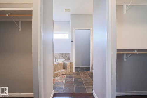 Hallway with wood flooring leading to a bathroom featuring a corner bathtub with tile surround, a window, and tiled flooring - 205 79 Street Sw, Edmonton, AB - Indoor