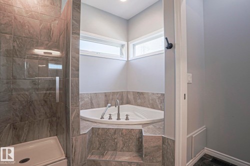 This bathroom features a corner soaking tub with a tiled surround, a separate glass-enclosed shower, and windows providing natural light - 205 79 Street Sw, Edmonton, AB - Indoor Photo Showing Bathroom