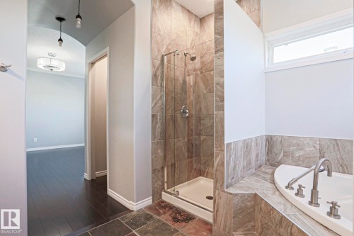 Bathroom featuring a corner soaking tub with a deck-mounted faucet, a glass-enclosed shower with tiled walls, and a window providing natural light - 205 79 Street Sw, Edmonton, AB - Indoor Photo Showing Bathroom
