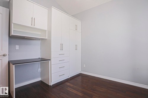 This room features dark hardwood flooring, white built-in cabinetry with silver hardware, and a dedicated desk area with overhead storage - 205 79 Street Sw, Edmonton, AB - Indoor Photo Showing Other Room
