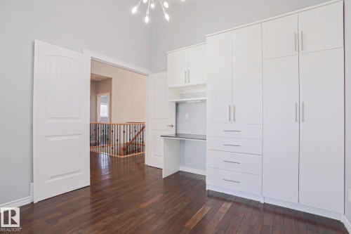 This room features dark hardwood flooring, white built-in cabinetry with a desk area, and an entryway with white double doors - 205 79 Street Sw, Edmonton, AB - Indoor Photo Showing Other Room