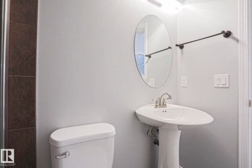 Well-appointed bathroom featuring a pedestal sink with a brushed nickel faucet, an oval wall mirror, and a towel bar - 205 79 Street Sw, Edmonton, AB - Indoor Photo Showing Bathroom