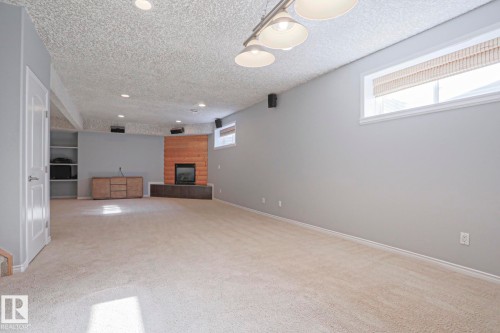 This spacious room features light-colored carpeting, light grey walls, and a fireplace with a wood-paneled surround - 205 79 Street Sw, Edmonton, AB - Indoor Photo Showing Other Room With Fireplace