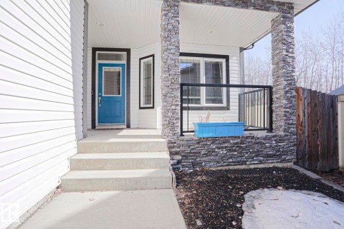 The property features a welcoming front entrance with a blue door, white siding, and stone veneer accents - 205 79 Street Sw, Edmonton, AB - Outdoor With Exterior