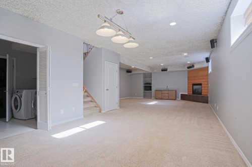 Spacious room featuring light-colored carpet, a fireplace with a wood-paneled surround, and built-in shelving - 205 79 Street Sw, Edmonton, AB - Indoor