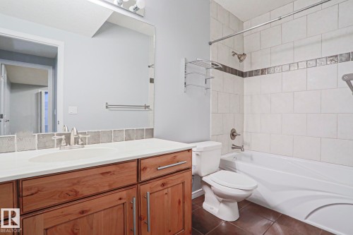 The bathroom features a wooden vanity with a white countertop and an integrated sink, complemented by a large mirror and overhead lighting - 205 79 Street Sw, Edmonton, AB - Indoor Photo Showing Bathroom