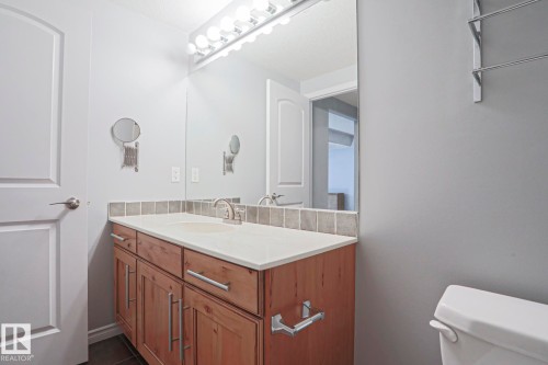 Bathroom vanity featuring a light wood cabinet with brushed nickel hardware, a light-colored countertop, and a tiled backsplash - 205 79 Street Sw, Edmonton, AB - Indoor Photo Showing Bathroom