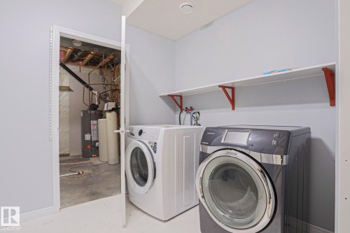 Dedicated laundry space featuring a white shelf with red brackets, light grey walls, and a white floor - 205 79 Street Sw, Edmonton, AB - Indoor Photo Showing Laundry Room