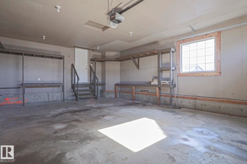 This spacious garage features a concrete floor, built-in shelving, a window, and a door with stairs for direct access - 205 79 Street Sw, Edmonton, AB - Indoor Photo Showing Garage