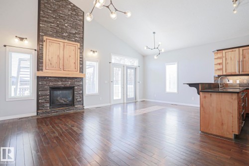 This expansive living area features hardwood floors, a stone fireplace with a wooden mantel, and vaulted ceilings - 205 79 Street Sw, Edmonton, AB - Indoor With Fireplace