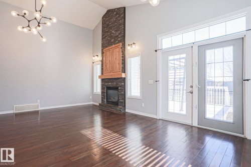 Spacious living area featuring high vaulted ceilings, a prominent stone fireplace with a wooden mantel, and rich hardwood flooring - 205 79 Street Sw, Edmonton, AB - Indoor Photo Showing Living Room With Fireplace