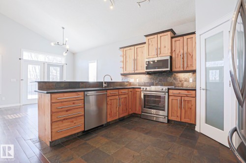 The kitchen features wood cabinetry, stainless steel appliances, and dark stone countertops - 205 79 Street Sw, Edmonton, AB - Indoor Photo Showing Kitchen