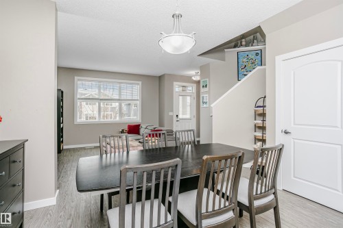 The property features an open-concept living area with a dining space, showcasing a contemporary light fixture, a large window with horizontal blinds, and a white interior door - 6116 Rosenthal Way, Edmonton, AB - Indoor Photo Showing Dining Room