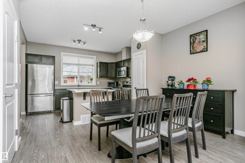 The property features an open-concept dining area and kitchen with dark wood flooring, light gray walls, and white trim - 6116 Rosenthal Way, Edmonton, AB - Indoor Photo Showing Dining Room