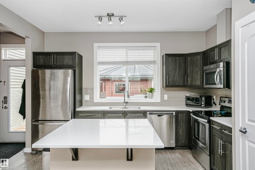 The kitchen features dark wood cabinetry, stainless steel appliances, a white island with a countertop, and a window above the sink - 6116 Rosenthal Way, Edmonton, AB - Indoor Photo Showing Kitchen With Stainless Steel Kitchen With Upgraded Kitchen