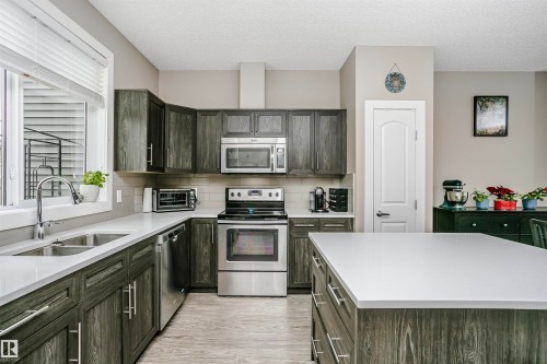 The kitchen features dark wood cabinetry, stainless steel appliances, and light countertops - 6116 Rosenthal Way, Edmonton, AB - Indoor Photo Showing Kitchen With Stainless Steel Kitchen With Double Sink