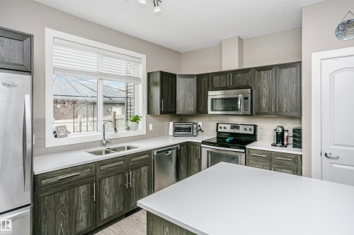 Kitchen featuring dark wood cabinetry, light countertops, stainless steel appliances, and a window above the sink - 6116 Rosenthal Way, Edmonton, AB - Indoor Photo Showing Kitchen With Stainless Steel Kitchen With Double Sink