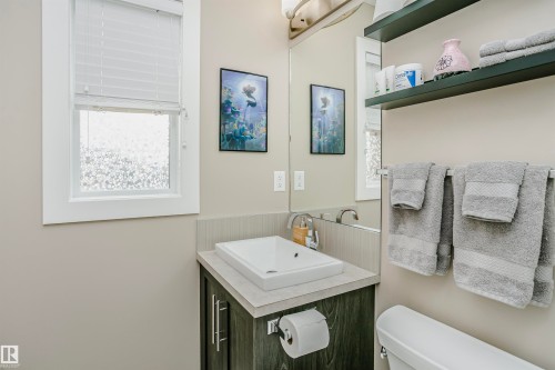 This bathroom features a window with white blinds, a vanity with a rectangular vessel sink and a modern faucet, and sleek shelving for storage - 6116 Rosenthal Way, Edmonton, AB - Indoor Photo Showing Bathroom