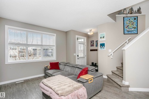 Living area featuring a large window with blinds, light gray walls, and wood-look flooring - 6116 Rosenthal Way, Edmonton, AB - Indoor Photo Showing Living Room