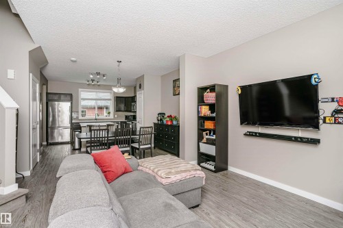 Open concept living area with grey flooring, a grey sectional sofa, and a wall-mounted flat-screen television - 6116 Rosenthal Way, Edmonton, AB - Indoor Photo Showing Living Room