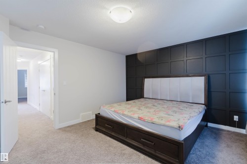 Bedroom featuring a decorative accent wall with paneling, light grey carpeting, and a flush mount ceiling light - 2878 Koshal Crescent, Edmonton, AB - Indoor Photo Showing Bedroom