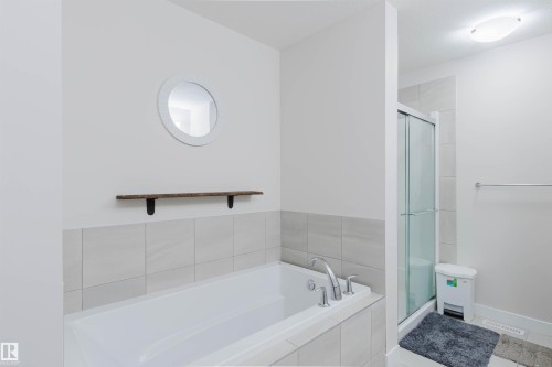 Bathroom featuring a built-in bathtub with chrome fixtures, a glass-enclosed shower, and light-toned wall tiling - 2878 Koshal Crescent, Edmonton, AB - Indoor Photo Showing Bathroom