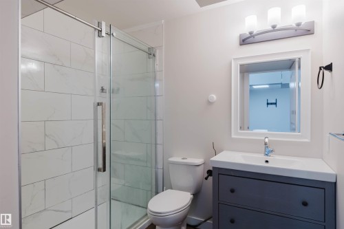 Bathroom featuring a white tiled shower with a glass door, a toilet, and a vanity with a white countertop and a mirror - 2878 Koshal Crescent, Edmonton, AB - Indoor Photo Showing Bathroom