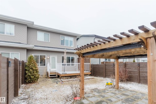 The property features a wooden deck with white railings, accessed via a door, and a wooden pergola covering a paved patio area - 2878 Koshal Crescent, Edmonton, AB - Outdoor