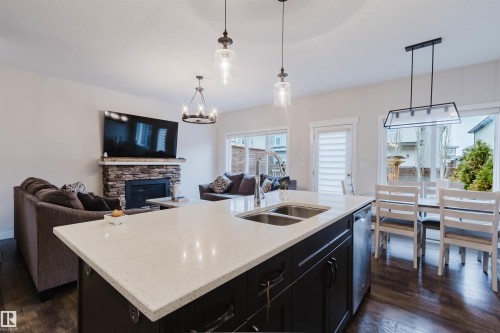 This property features a modern kitchen island with a light-colored countertop and double sink, hardwood flooring throughout, and a living area with a stone fireplace - 2878 Koshal Crescent, Edmonton, AB - Indoor Photo Showing Kitchen With Fireplace With Double Sink