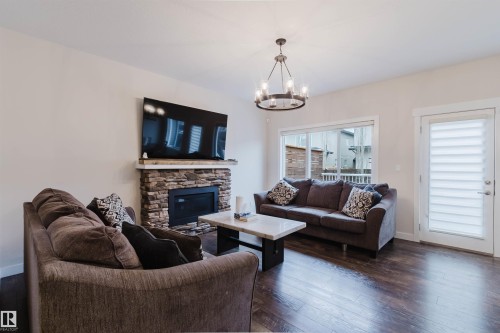 Living area featuring dark hardwood floors, a stone-faced fireplace with a natural wood mantel, and large windows providing natural light - 2878 Koshal Crescent, Edmonton, AB - Indoor Photo Showing Living Room With Fireplace