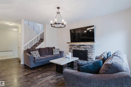 Living room featuring dark wood style flooring, a staircase with white risers and handrails, and a stacked stone fireplace with a wood mantel - 2878 Koshal Crescent, Edmonton, AB - Indoor Photo Showing Living Room With Fireplace