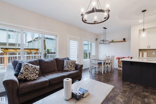 Open concept living space featuring dark wood-style flooring, ample natural light from large windows, and a modern dining area with a chandelier - 2878 Koshal Crescent, Edmonton, AB - Indoor Photo Showing Living Room