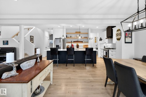 This property features an open-concept living area with light wood flooring, a kitchen island with seating, white cabinetry, and a staircase with a wooden handrail - 345 Meadowview Drive, Fort Saskatchewan, AB - Indoor