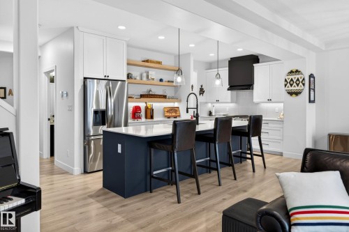 The kitchen features a dark blue island with seating, a stainless steel refrigerator, a black hood fan, and white cabinetry - 345 Meadowview Drive, Fort Saskatchewan, AB - Indoor Photo Showing Kitchen With Upgraded Kitchen