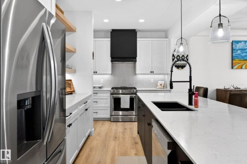 The kitchen features stainless steel appliances, including a refrigerator and range, a black range hood, and light wood flooring - 345 Meadowview Drive, Fort Saskatchewan, AB - Indoor Photo Showing Kitchen With Double Sink With Upgraded Kitchen