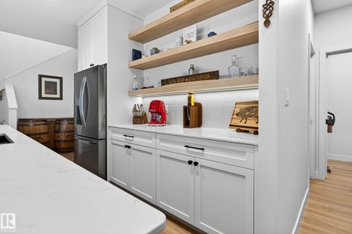 This kitchen features white cabinetry with black hardware, a stainless steel refrigerator, and light wood open shelving - 345 Meadowview Drive, Fort Saskatchewan, AB - Indoor
