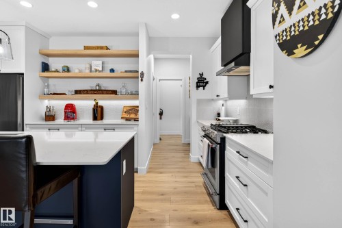 The kitchen features white cabinetry, a dark blue island with a white countertop, and light hardwood flooring - 345 Meadowview Drive, Fort Saskatchewan, AB - Indoor Photo Showing Kitchen With Upgraded Kitchen