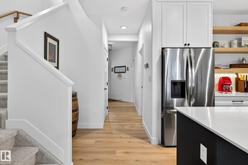 The kitchen features a stainless steel refrigerator, white upper cabinetry, and open wooden shelving - 345 Meadowview Drive, Fort Saskatchewan, AB - Indoor