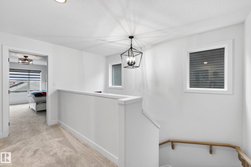 The property features a bright hallway with white walls, carpeted flooring, and a modern geometric pendant light fixture - 345 Meadowview Drive, Fort Saskatchewan, AB - Indoor Photo Showing Other Room