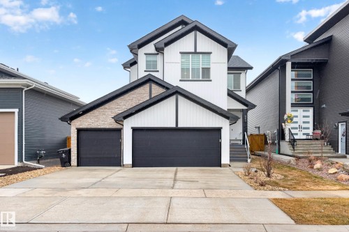 The property features a two-car garage with black doors, a white facade with black trim, and stone accents - 345 Meadowview Drive, Fort Saskatchewan, AB - Outdoor