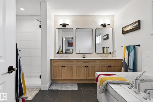 The bathroom features a double vanity with light wood cabinetry, two framed mirrors, and black sconces - 345 Meadowview Drive, Fort Saskatchewan, AB - Indoor Photo Showing Bathroom