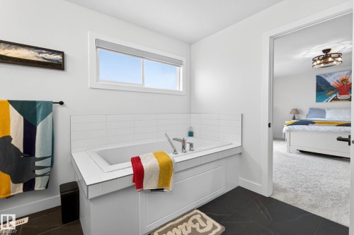 The bathroom features a built-in bathtub with white tile surround, dark tile flooring, and a window providing natural light - 345 Meadowview Drive, Fort Saskatchewan, AB - Indoor Photo Showing Bathroom