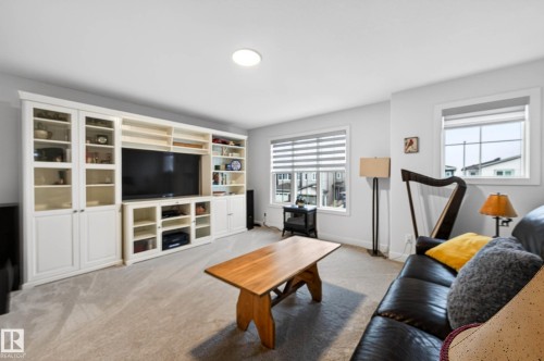 Living area featuring a built-in media unit with glass-front cabinets, light-colored carpeting, and windows fitted with blinds - 345 Meadowview Drive, Fort Saskatchewan, AB - Indoor Photo Showing Living Room