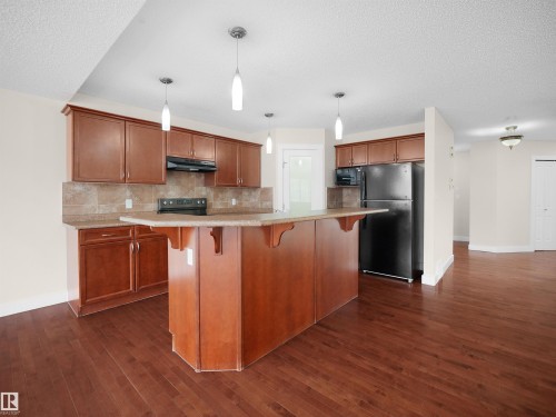 The kitchen features rich wood cabinetry, a tiled backsplash, and pendant lighting - 8361 Shaske Crescent, Edmonton, AB - Indoor Photo Showing Kitchen