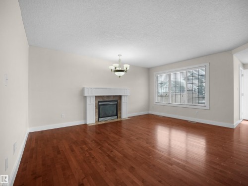 Bright living area featuring hardwood floors, a fireplace with a white mantel and stone surround, and a window with blinds - 8361 Shaske Crescent, Edmonton, AB - Indoor Photo Showing Living Room With Fireplace