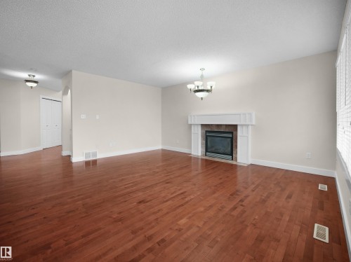 Spacious living area featuring hardwood flooring, a fireplace with a decorative mantel, and neutral-toned walls - 8361 Shaske Crescent, Edmonton, AB - Indoor Photo Showing Living Room With Fireplace